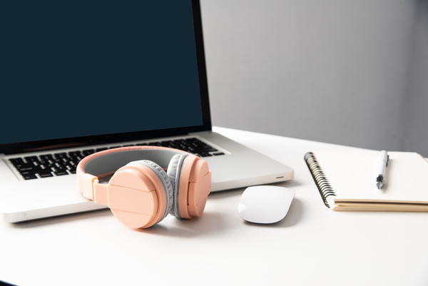 The image shows a laptop computer, a mouse and some headphones on a work desk.